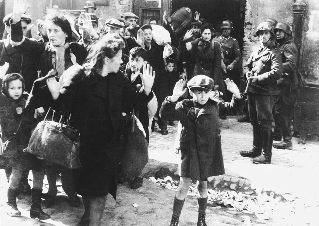 O menino, na frente, com as mãos para cima, enquanto é intimidado pelo soldado Josef Blösche, com uma submetralhadora, ao fundo.