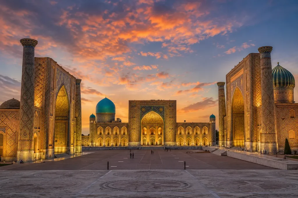 Praça do Registan em Samarcanda iluminada ao entardecer, mostrando a monumental arquitetura herdada do período timurida.