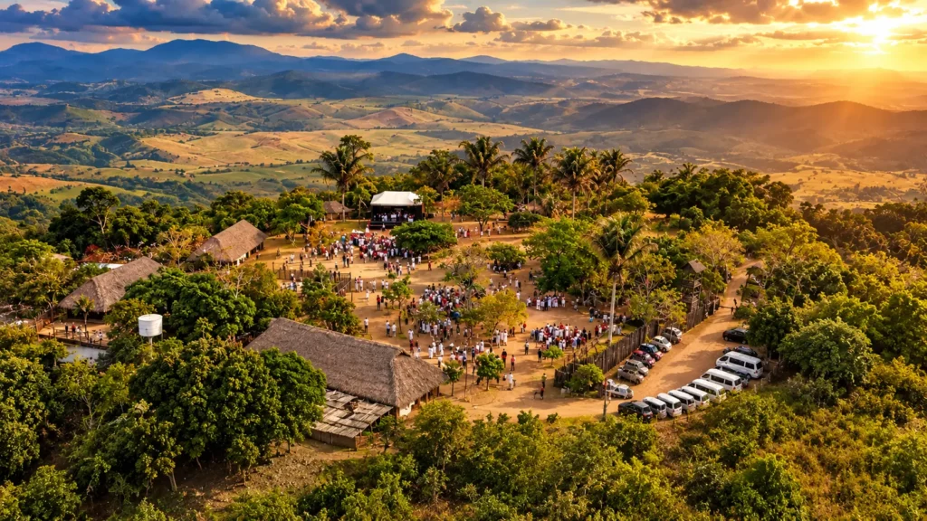 Vista aérea do Parque Memorial Quilombo dos Palmares na Serra da Barriga ao pôr do sol, mostrando réplicas de habitações rústicas e visitantes reunidos.